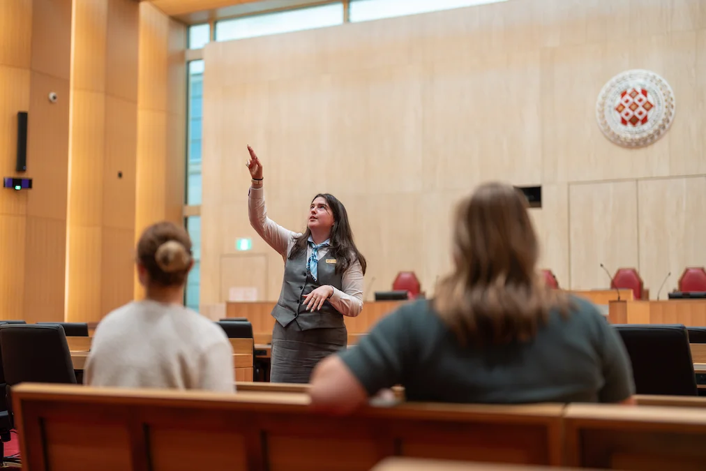 Two visitors listen to a guide interpreter in the courtroom